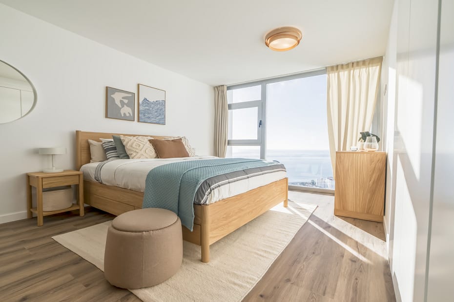 Fotografía de arquitectura de un dormitorio principal moderno en Almuñécar con cama de madera, luz natural y vistas panorámicas al mar Mediterráneo.